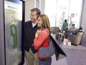 A man and a woman at a shopping mall looking at a map on an interactive smart kiosk