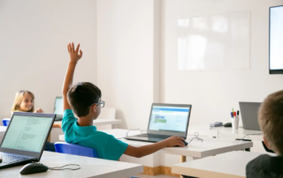 student raising hand while using laptop