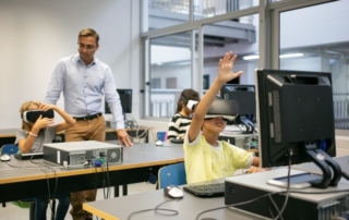 children in computer lab wearing VR headsets beside monitors