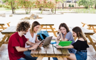 Students studying together with laptop at outdoor wooden benches