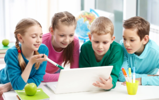four children gathered around a laptop learning together