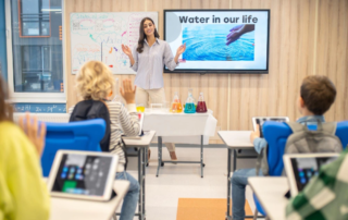 teacher presenting with wall mounted monitor and students using tablets