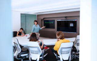presenter pointing at wall mounted monitors in conference room with chairs