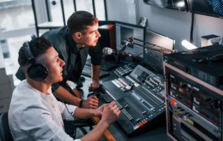 Two men operating audio mixer and microphone in studio