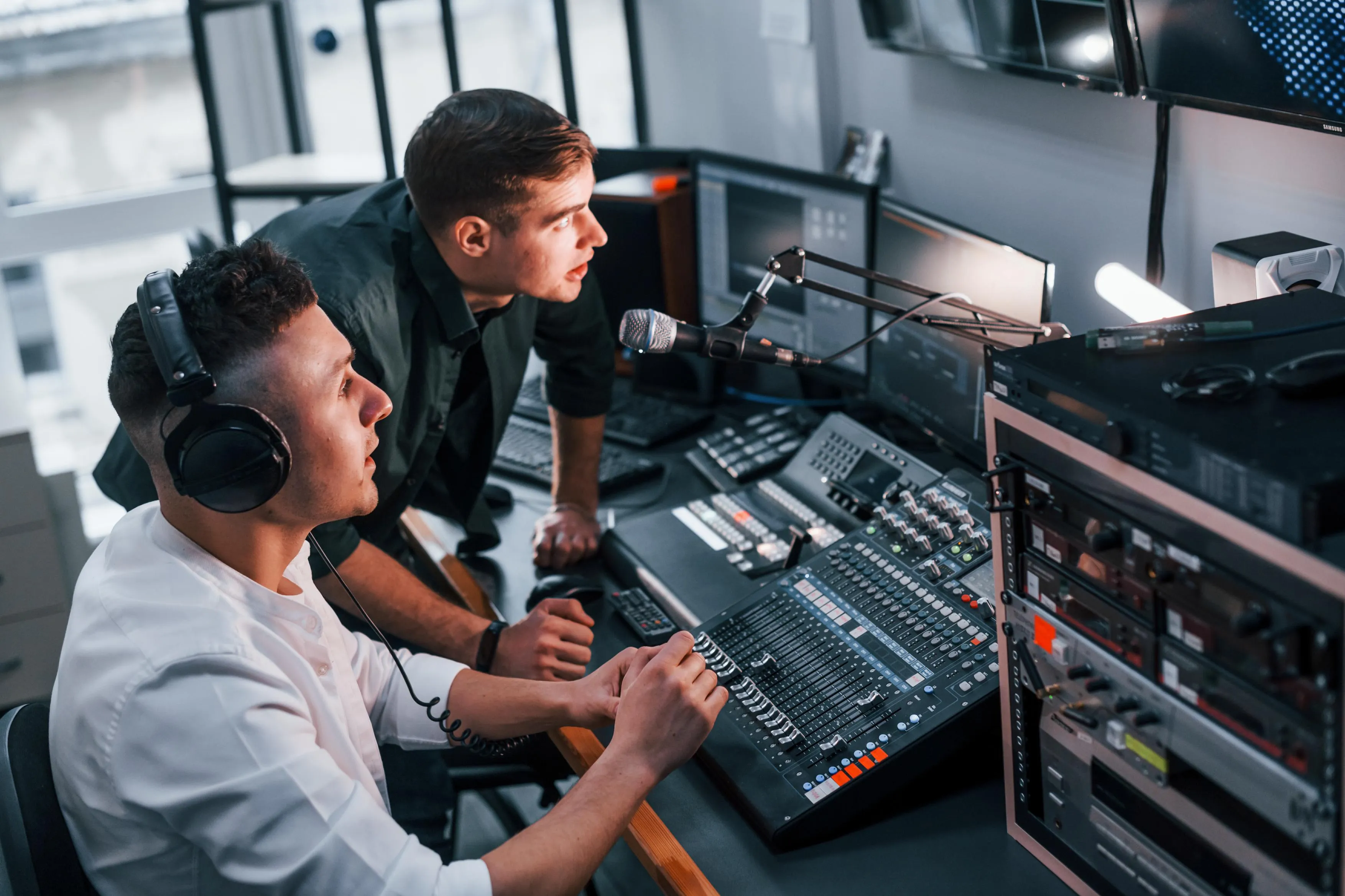 Two men operating audio mixer and microphone in studio