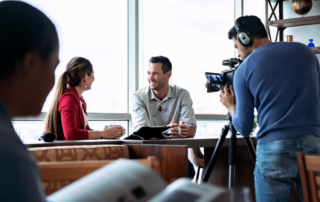 Makeup artist and producer preparing man on camera for filming