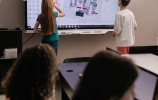 two students drawing on a classroom interactive whiteboard touchscreen