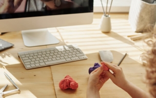 child molding colorful clay at wooden desk with iMac monitor keyboard and mouse