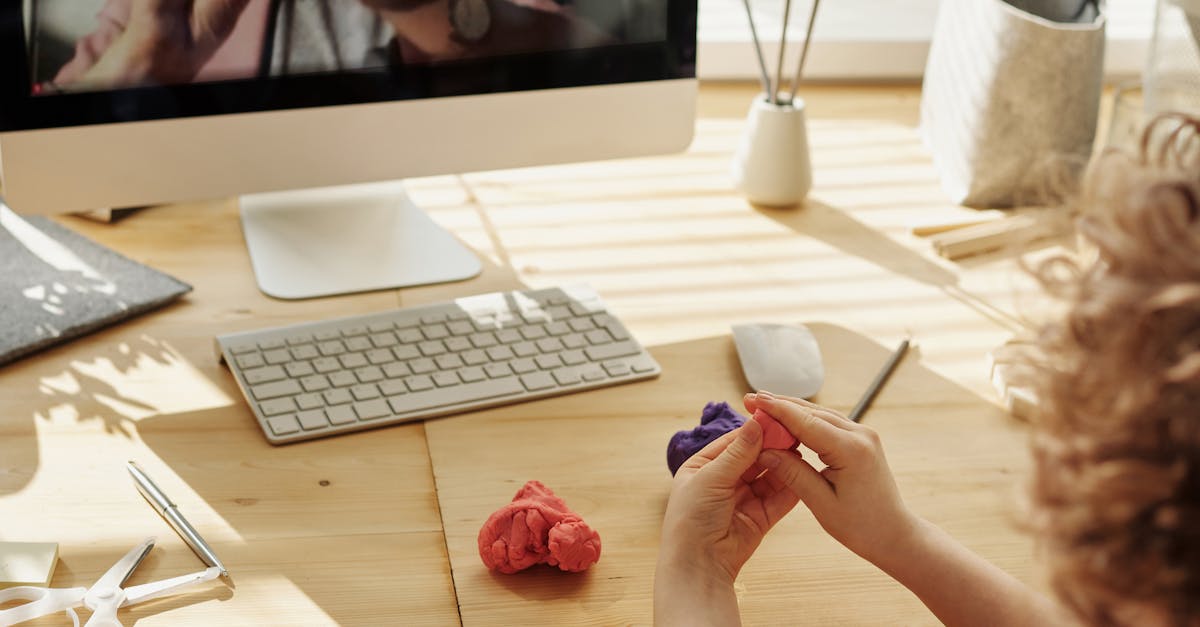child molding colorful clay at wooden desk with iMac monitor keyboard and mouse