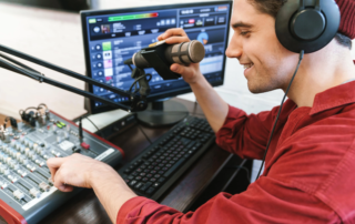 Man using microphone and audio console in front of computer monitor