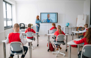 classroom with students facing teacher and wall mounted monitor