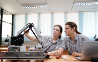 students operating robotic arm with laptop