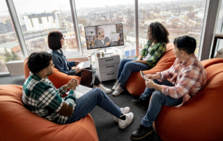 group on beanbag chairs watching video call on desktop monitor