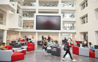 students gathered in atrium lounge with modular seating and wall mounted display
