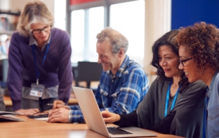 group of educators gathered around laptop in library device laptop