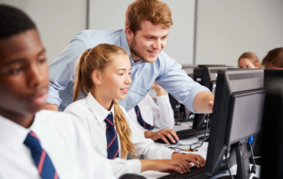 teacher assisting students on desktop computers