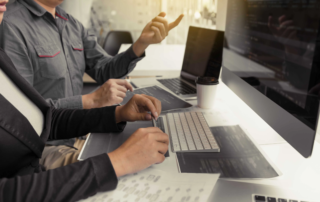 two people working at desk with desktop and laptops