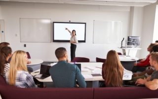 instructor pointing at wall monitor in classroom
