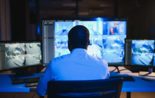 Man monitoring multiple security camera feeds on large monitors