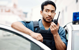 Police officer using walkie talkie beside patrol car