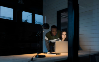 Two people working late at night on laptop in dark office