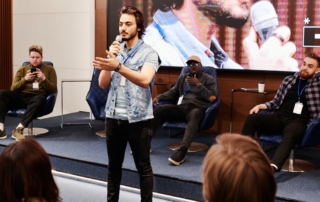 Speaker presenting with microphone in front of large monitor screen