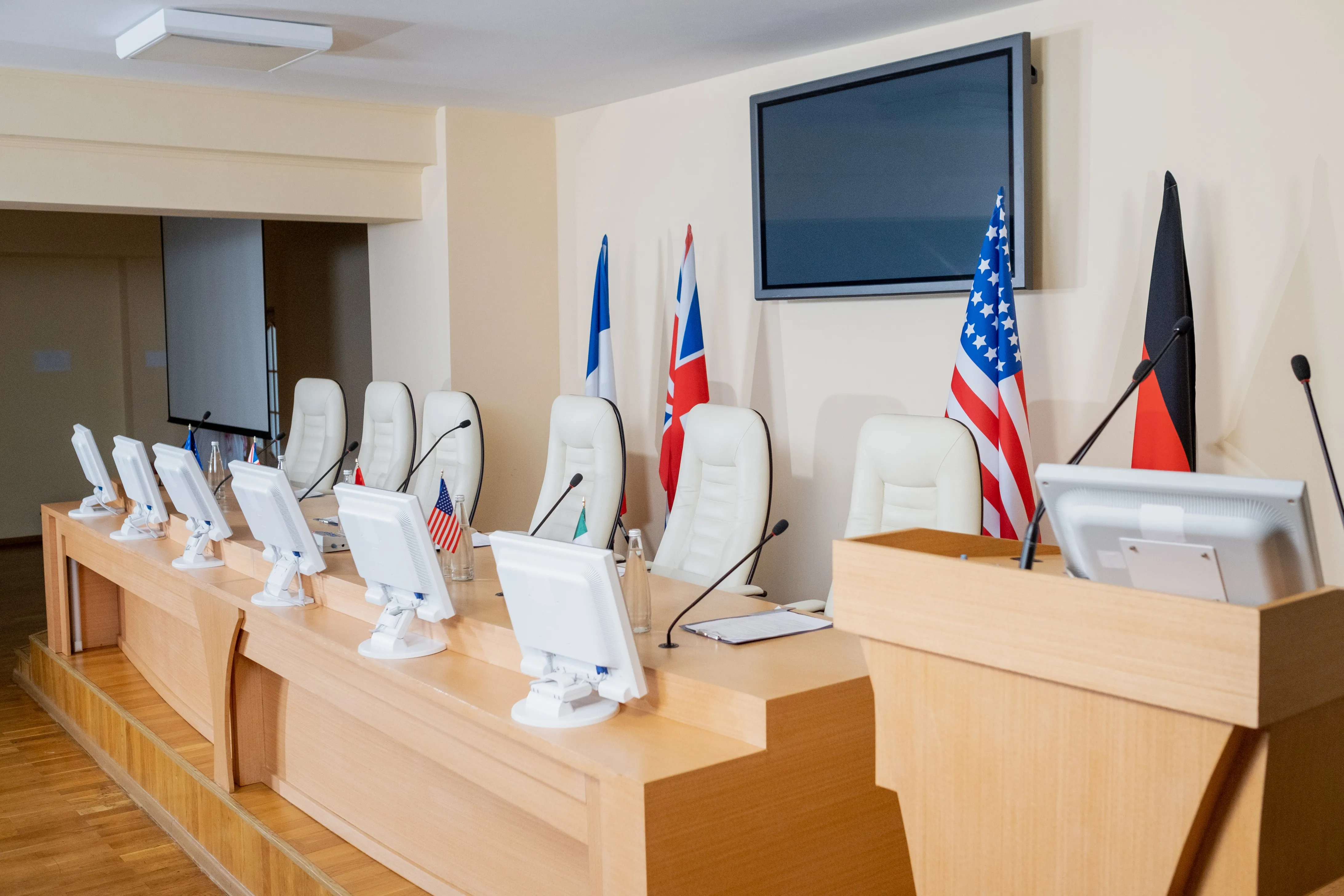 empty-conference-hall-with-row-of-microphones-com-2025-03-13-03-39-34-utc (1) International conference room with monitors microphones and national flags