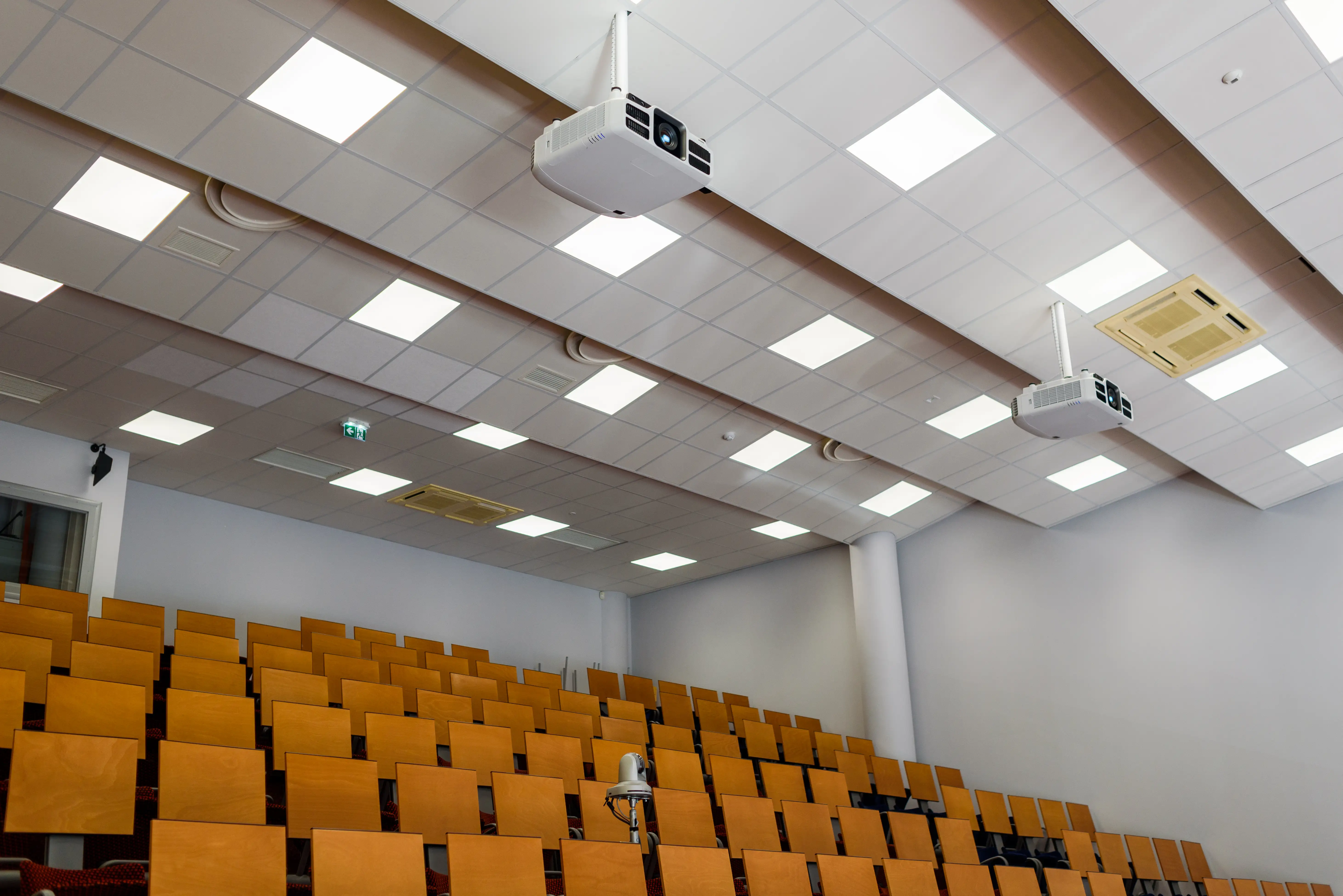 Empty lecture hall with ceiling mounted projectors and wooden seats