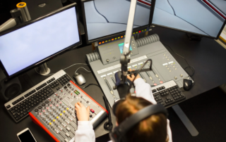Radio station setup with operator using mixing console and triple monitors