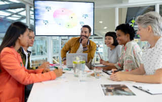 group of people at table with wall monitor and laptop device monitor laptop