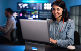 Woman smiling with headset while working on laptop in control room