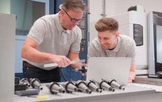 two engineers measuring metal part beside laptop device laptop