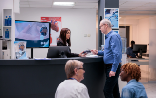 Man registering at medical front desk with monitor displaying health info