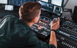 Man holding microphone in audio production studio with control panel and monitors