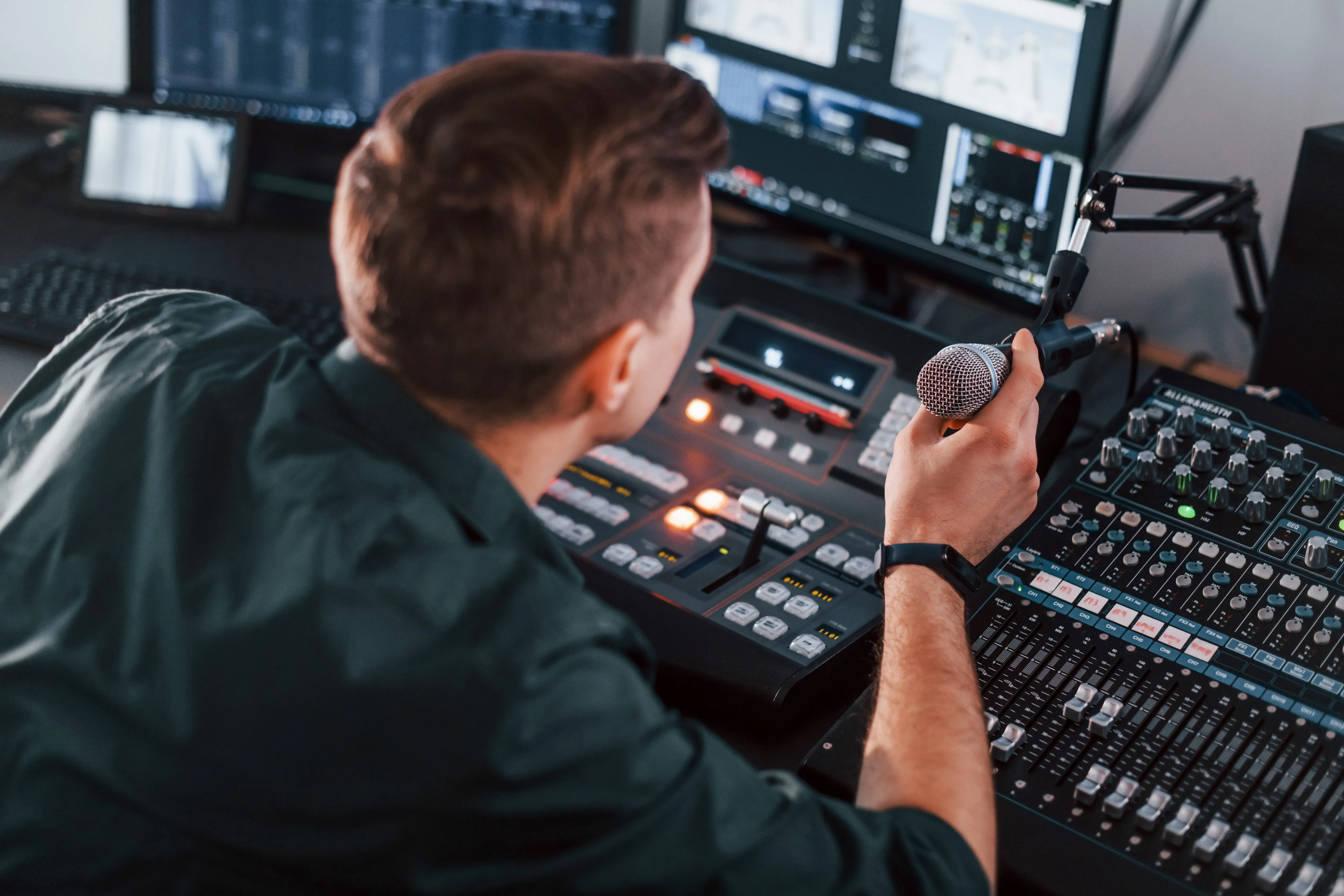 Man holding microphone in audio production studio with control panel and monitors