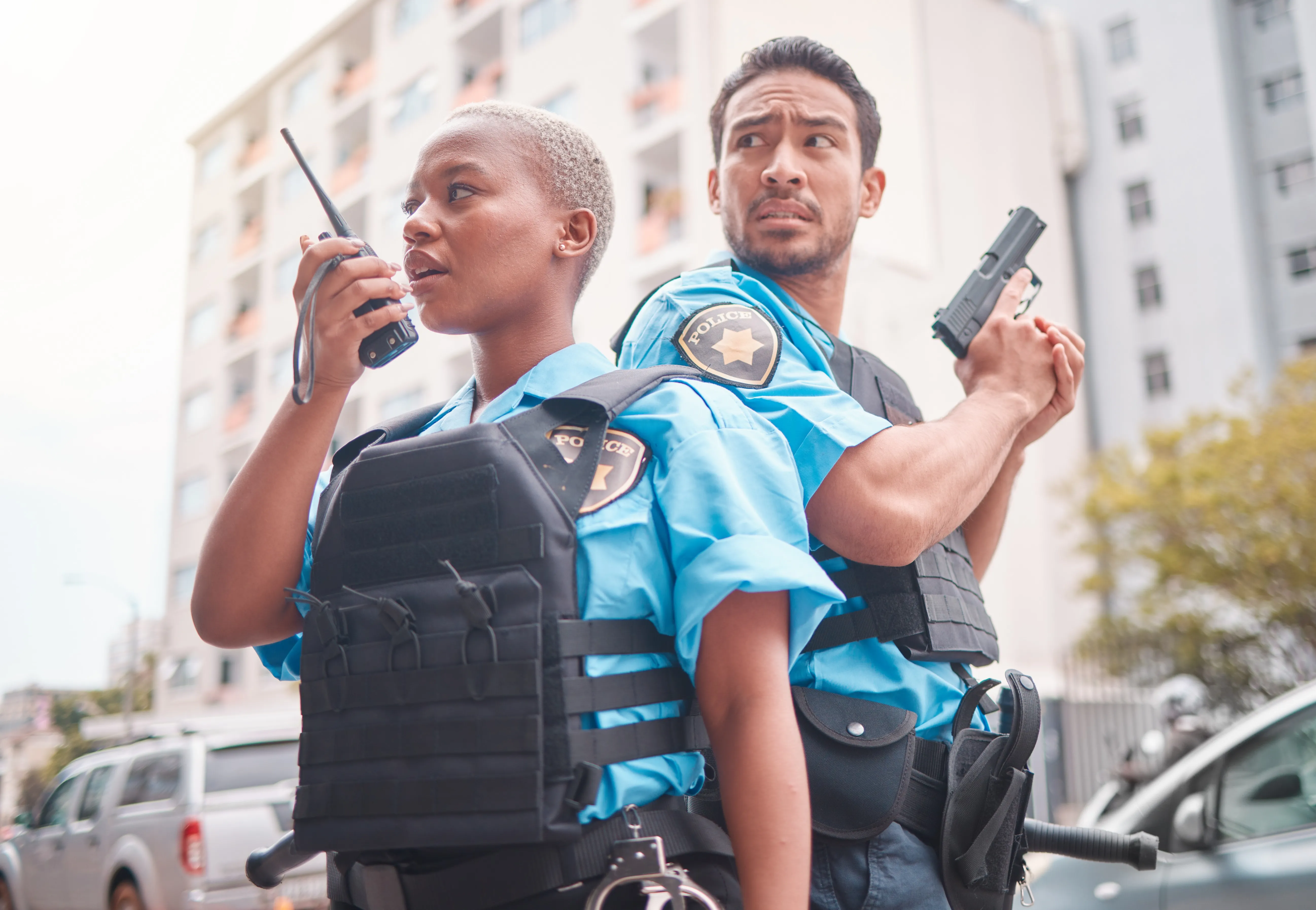 two officers back to back one holding radio device and one drawing handgun