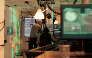 two coders in hoodies working at multiple monitors device monitors