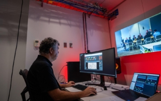 Operator in a control room with a curved monitor wall mounted screen laptop and camera equipment