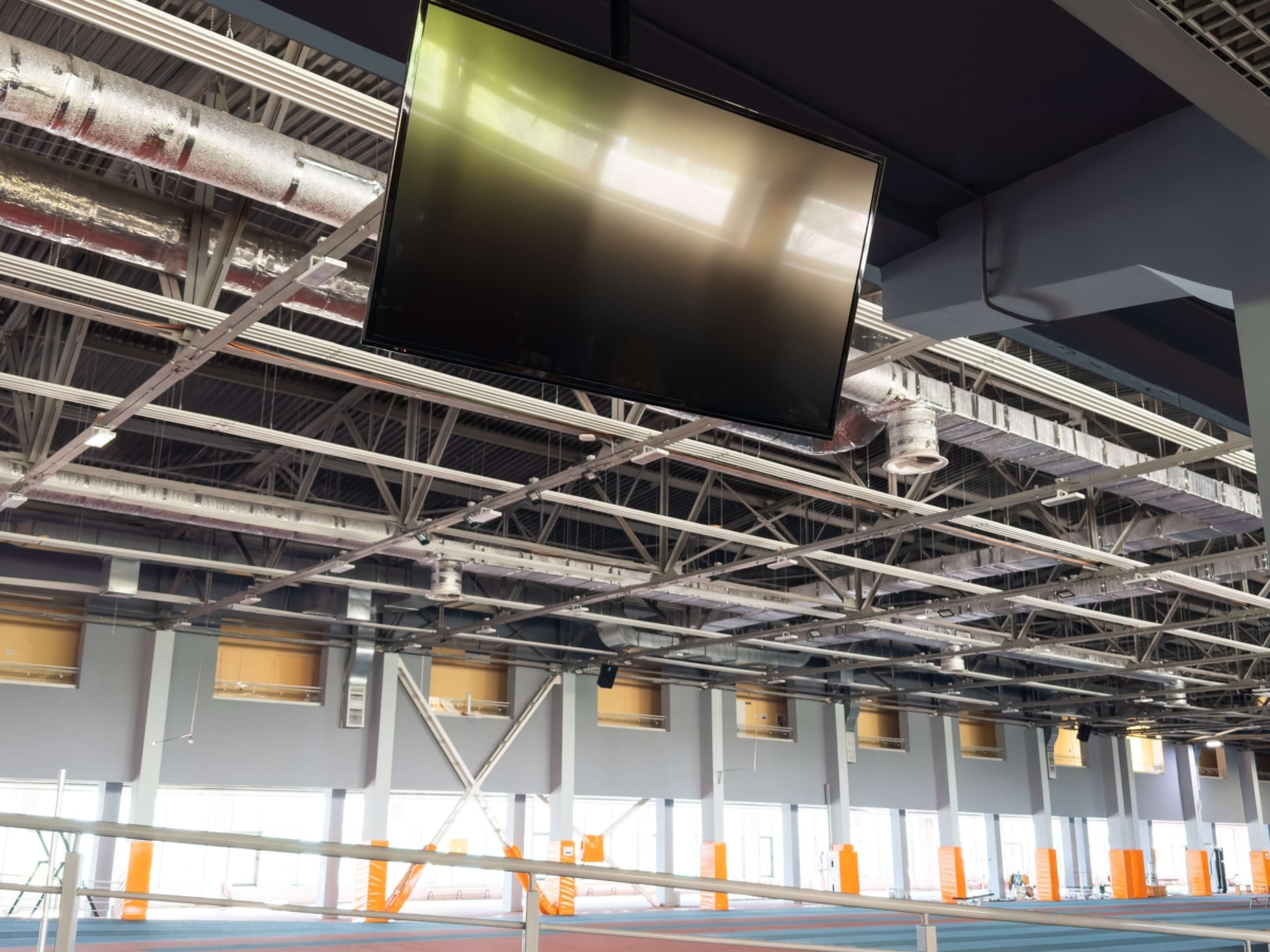 blank-lcd-screen-mock-up-in-subway-station-2025-01-10-05-00-12-utc (1) Overhead display screen suspended beneath steel truss ceiling with ventilation ducts visible