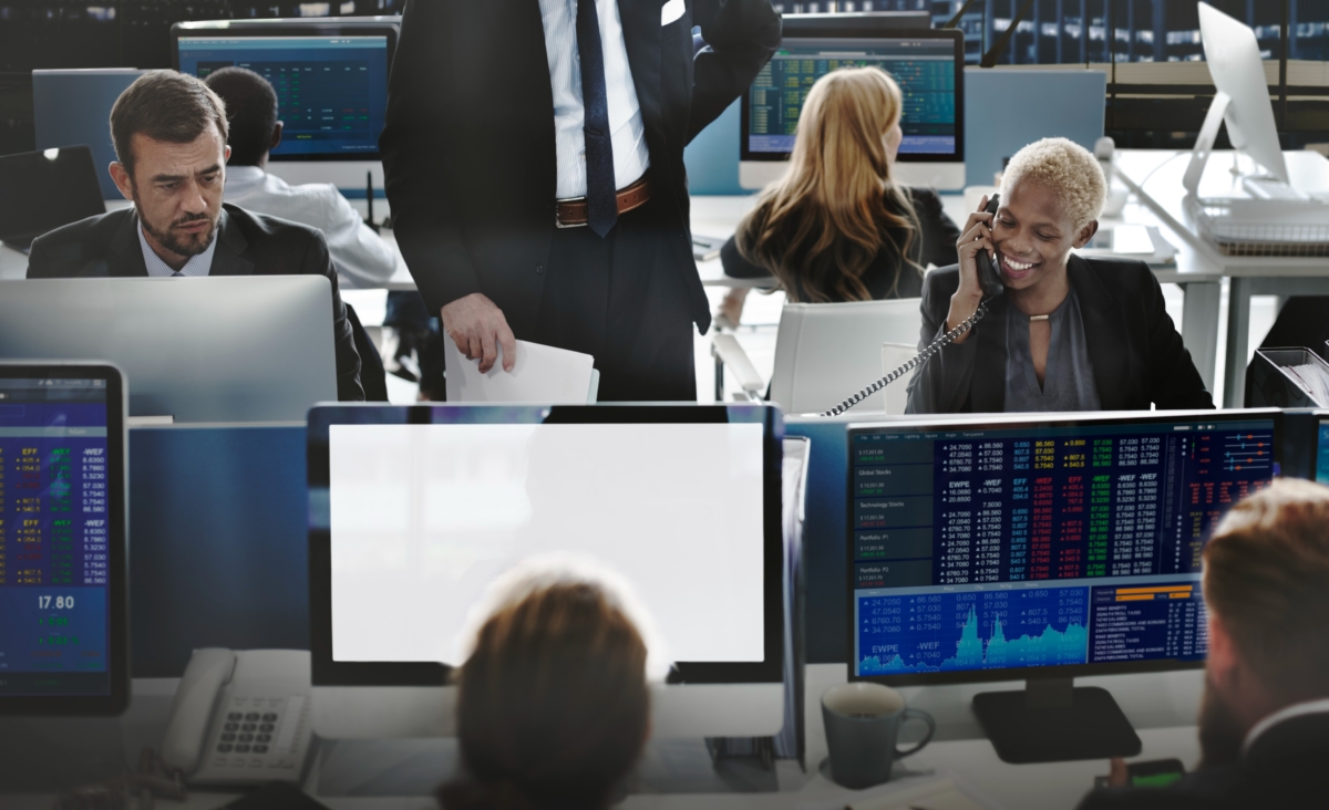 traders at open trading floor with multiple desktop monitors telephones and keyboards