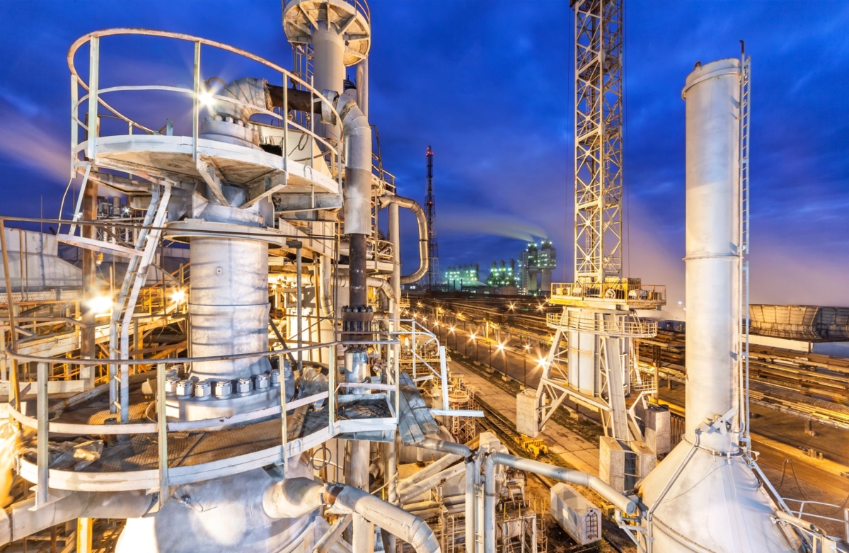 industrial refinery towers lit against deep blue sky with walkways and cameras