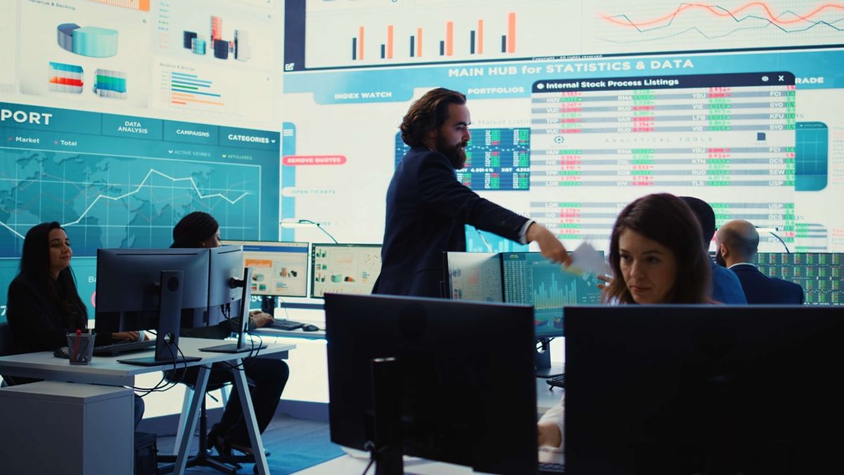 Presenter and participants at desks with multiple monitors videowall touchscreen and tablets