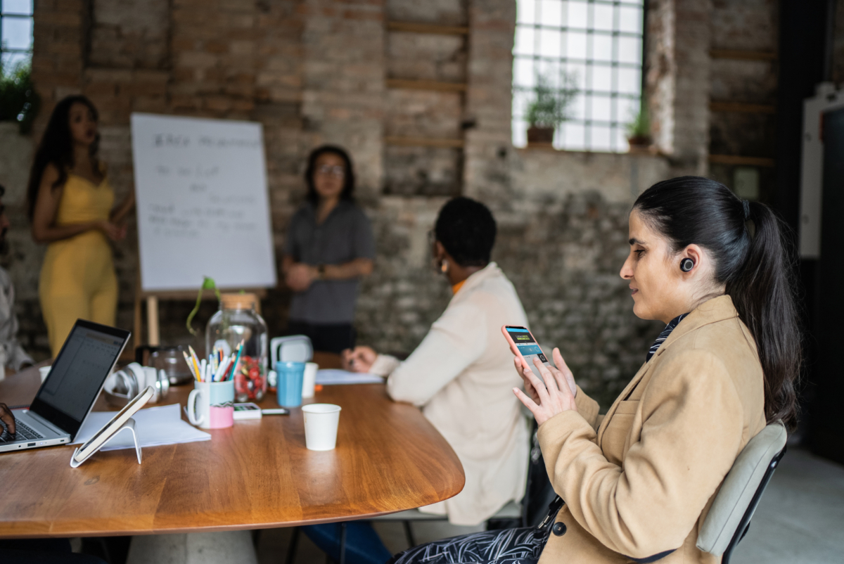 Visually impaired businesswoman using smartphone and earphones during business meeting